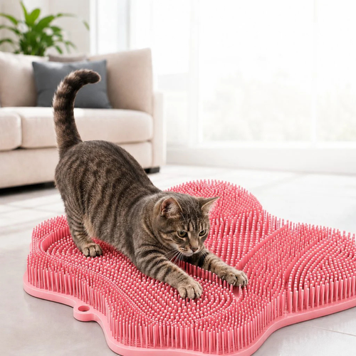 Cat scratching and grooming mat in pink with a tabby cat stretching on the bristles.