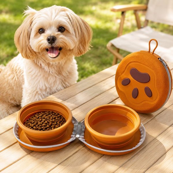 Collapsible double pet travel bowl in orange with food and water beside a small dog.