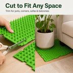 Green cat deterrent mat being trimmed with scissors to fit around a plant pot.