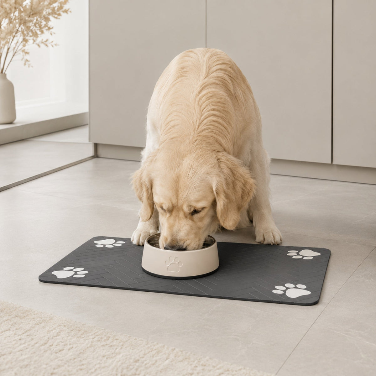 Paw print pet feeding mat in dark gray beneath a bowl used by a golden dog.