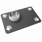 Paw print pet feeding mat in dark gray with a metal bowl on the herringbone surface.